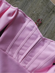 Close-up of a pink garment with pleated details on a wooden surface.