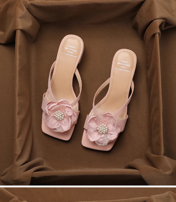 Pair of pink high-heeled sandals with floral decorations on a brown fabric background
