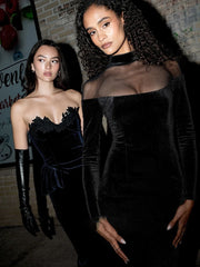 Two women in black dresses standing against a brick wall.