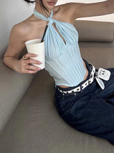Person wearing a light blue halter top and dark jeans, sitting on a couch holding a white cup.