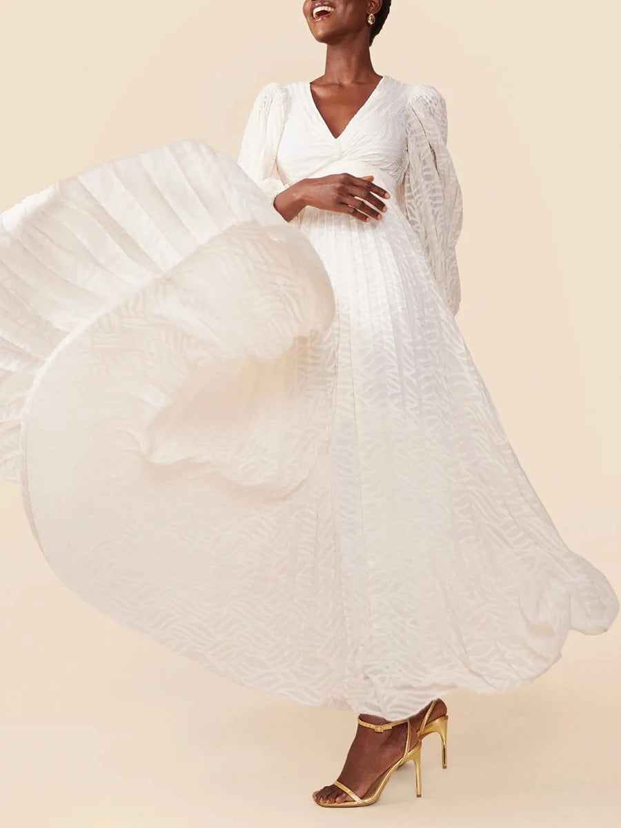 Woman wearing a flowing white dress with gold high-heeled shoes on a beige background