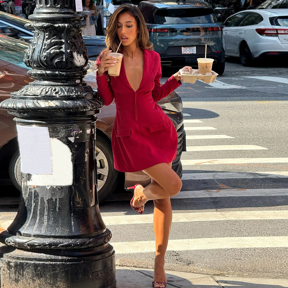 Woman in a red dress crossing a street holding drinks.