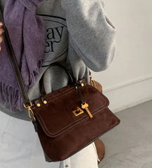Brown handbag held by a person wearing a gray sweater and purple scarf.