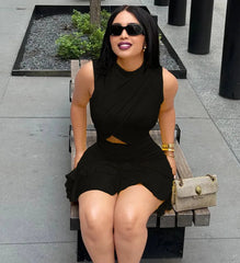Woman in a black dress sitting on a bench with sunglasses and a handbag.
