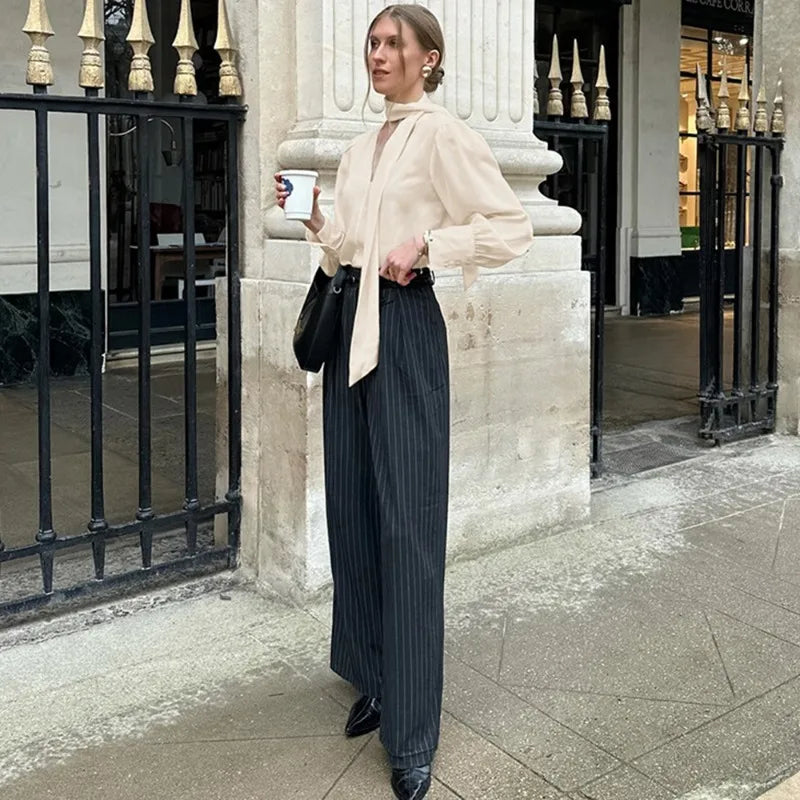 Woman in a beige blouse and dark striped pants standing on a city street.