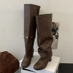 Brown knee-high boots on a white platform with a minimal background