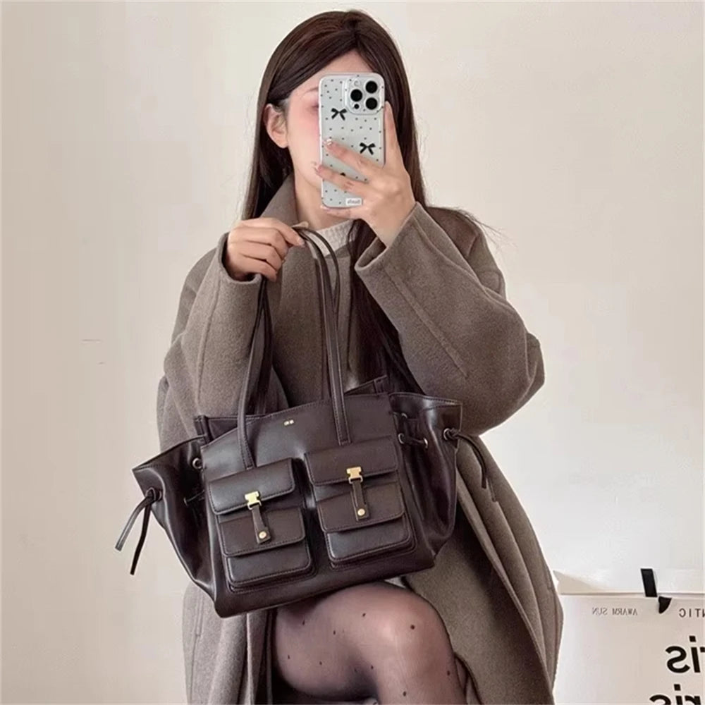 Person holding a dark brown leather handbag in front of a plain background