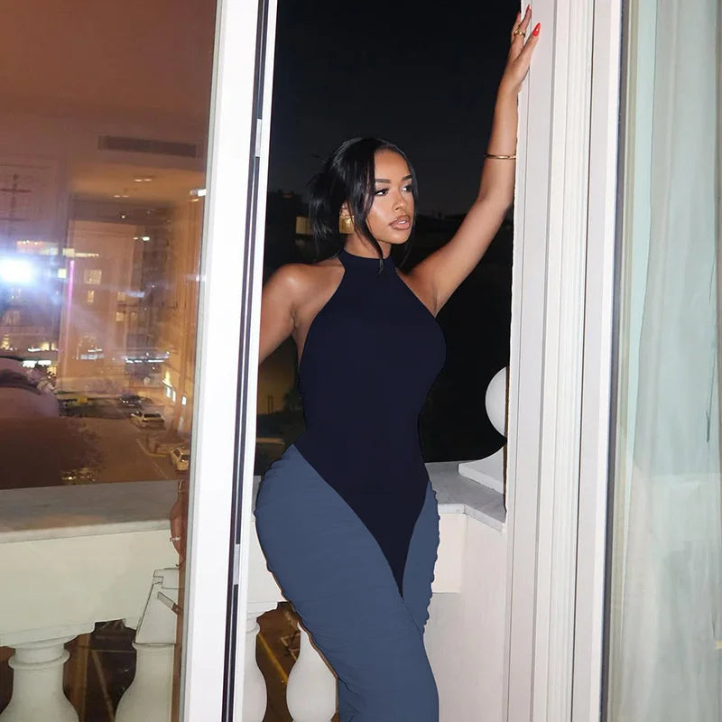 Woman in a navy blue outfit standing by a window with city lights visible outside.