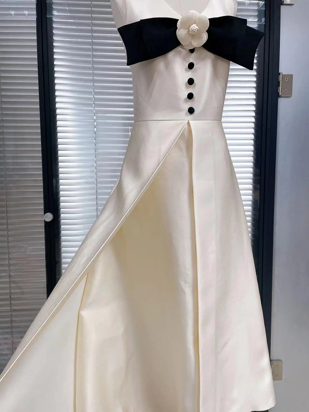 White evening gown with black bow and buttons against a neutral background