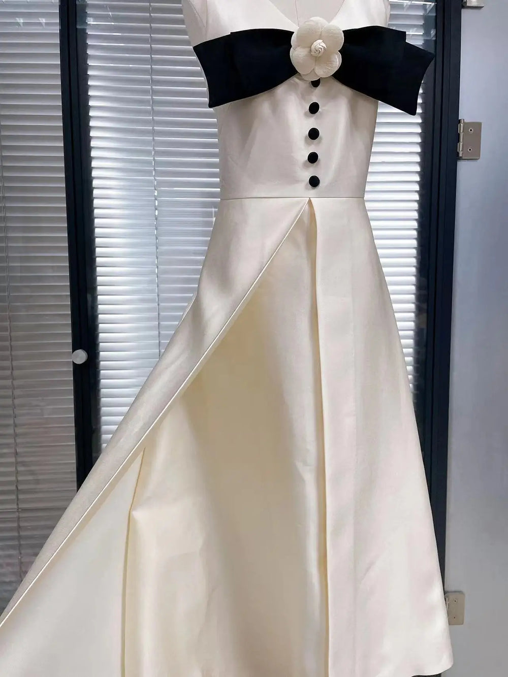 White evening gown with black bow and buttons against a neutral background