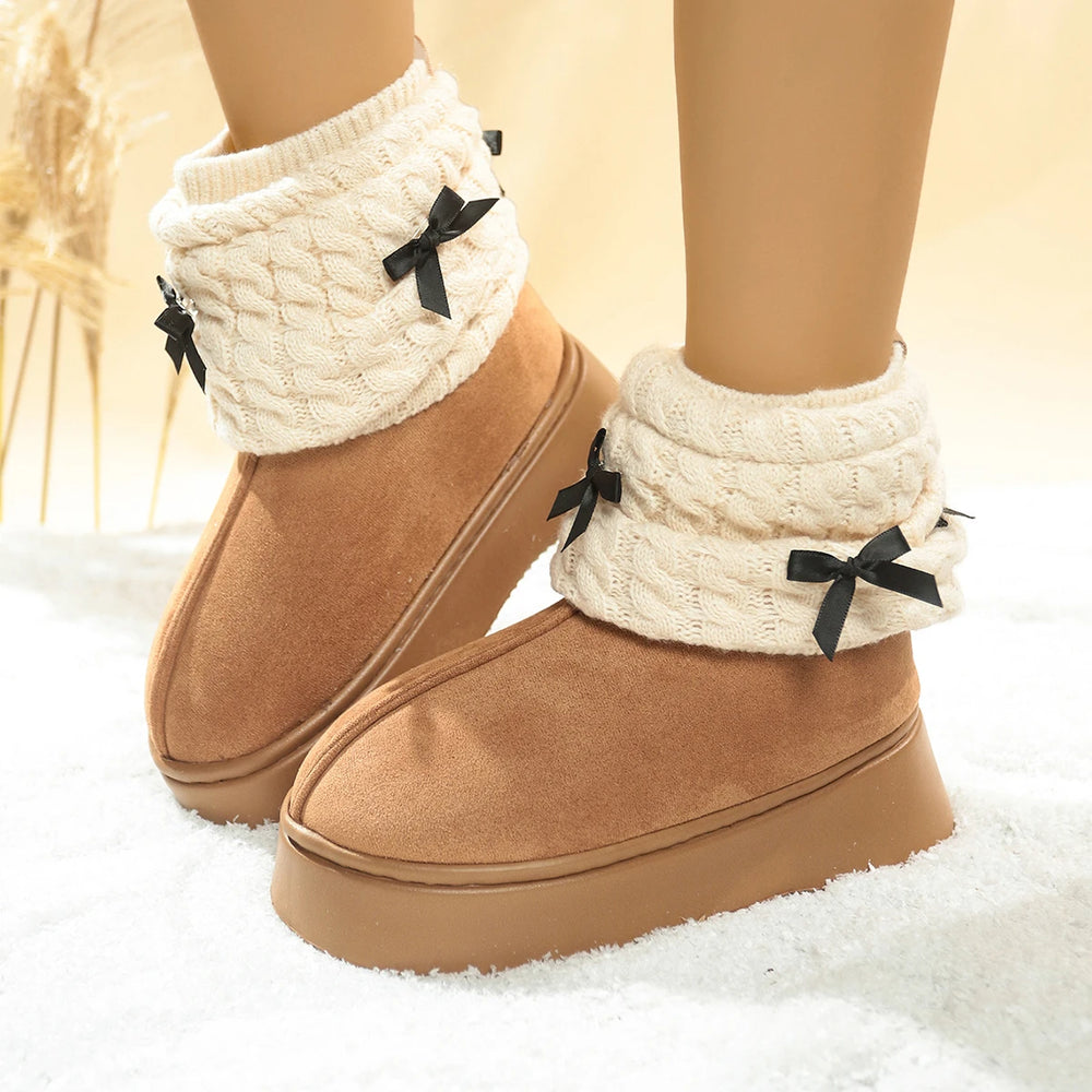 Brown boots with white knit leg warmers and black bows on a soft surface.