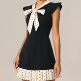 Black sleeveless top with a white polka dot bow and matching skirt on a neutral background