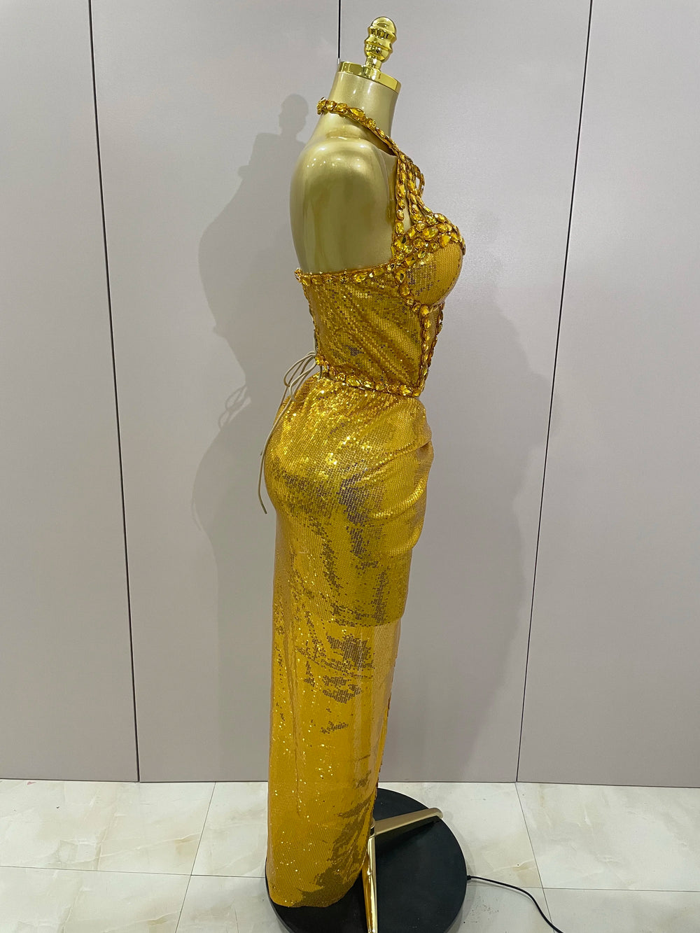 Gold evening gown on a mannequin against a plain background