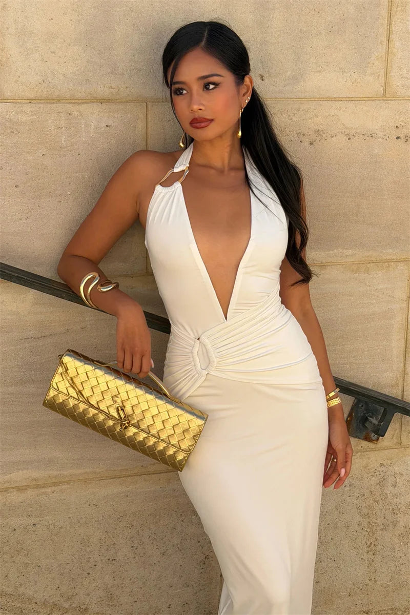 Woman in a white dress holding a gold clutch against a beige wall.