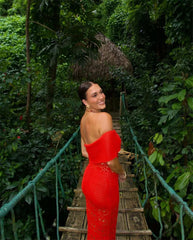 Woman in a red dress standing on a wooden bridge in a lush green forest.