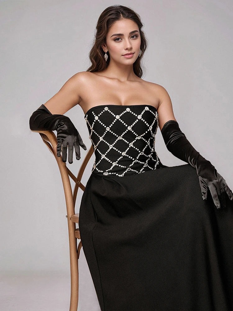 Woman in a black strapless gown with white embellishments and gloves, sitting on a chair against a gray background.
