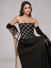 Woman in a black strapless gown with white embellishments and gloves, sitting on a chair against a gray background.