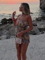 Woman in a floral dress standing on a rocky beach with sunset in the background