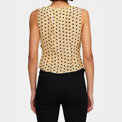 Woman wearing a beige sleeveless top with black polka dots and black pants on a white background