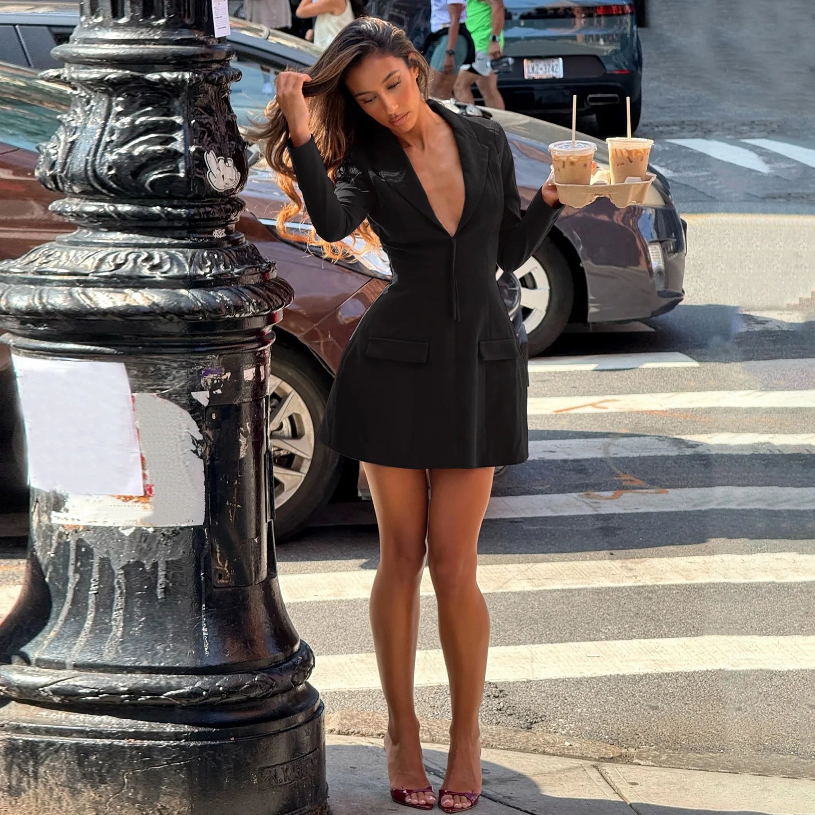 Woman in a black dress standing on a city street with a crosswalk.