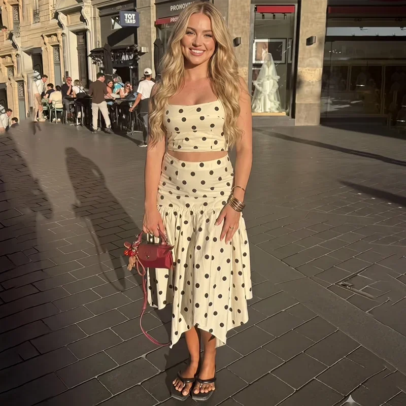 Full body shot of a woman in a white and black polka dot print crop top and asymmetrical midi skirt.