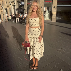 Full body shot of a woman in a white and black polka dot print crop top and asymmetrical midi skirt.