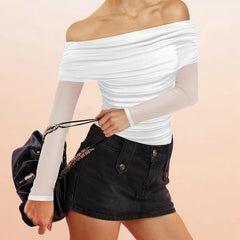 Person wearing a white off-shoulder top and black shorts holding a black handbag on a beige background