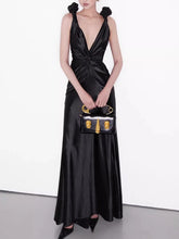 Woman in a black satin dress holding a matching handbag against a white background