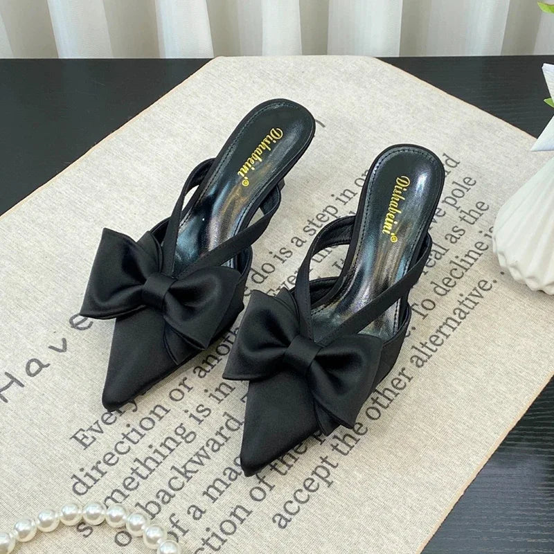 Black high-heeled shoes with bow details on a textured surface