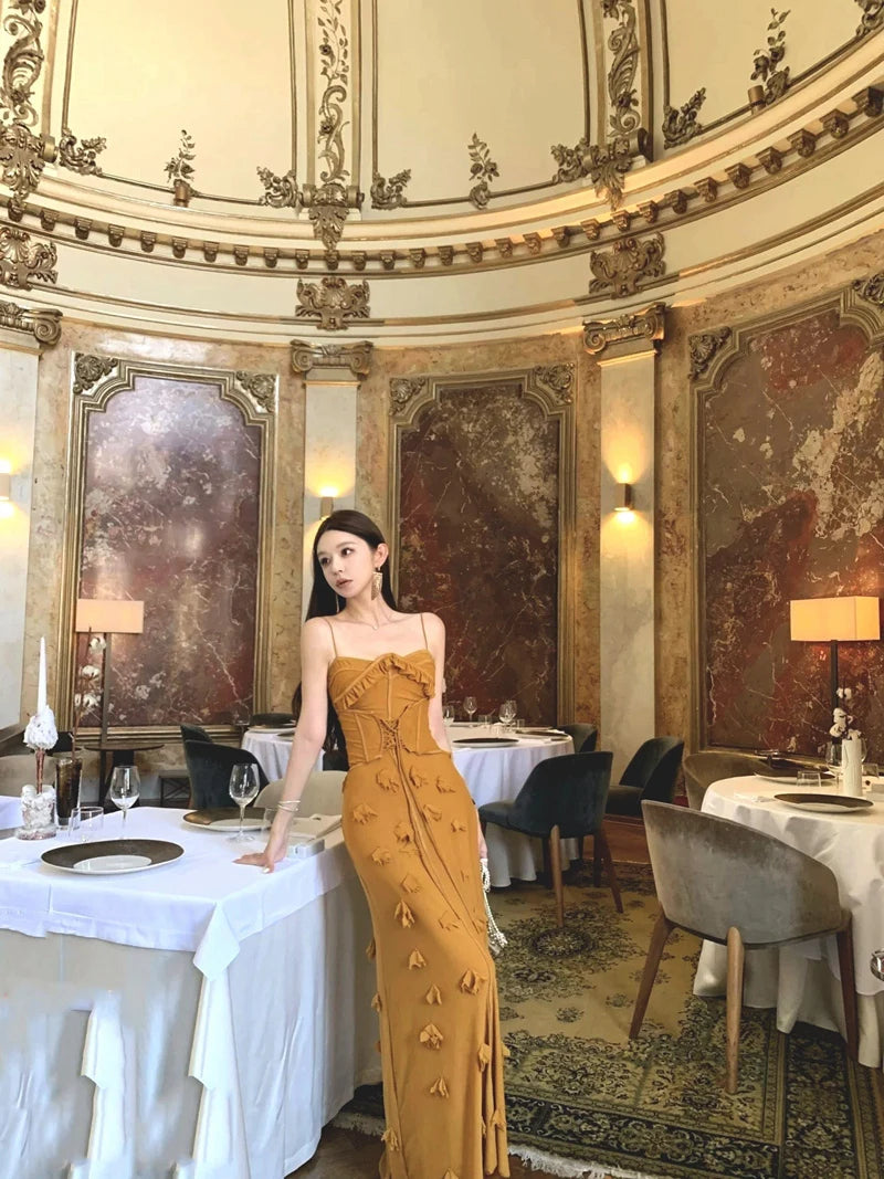Woman in a yellow dress standing in an ornate dining room with tables and chairs.