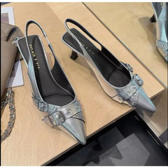 Silver high-heeled shoes with decorative buckles on a wooden surface