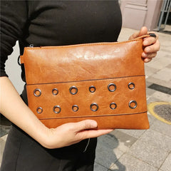 Brown leather clutch with grommet details held by a person on a city street.