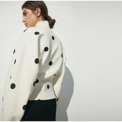 Person wearing a white sweater with black polka dots against a plain background