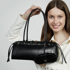 Woman holding a black handbag against a plain background