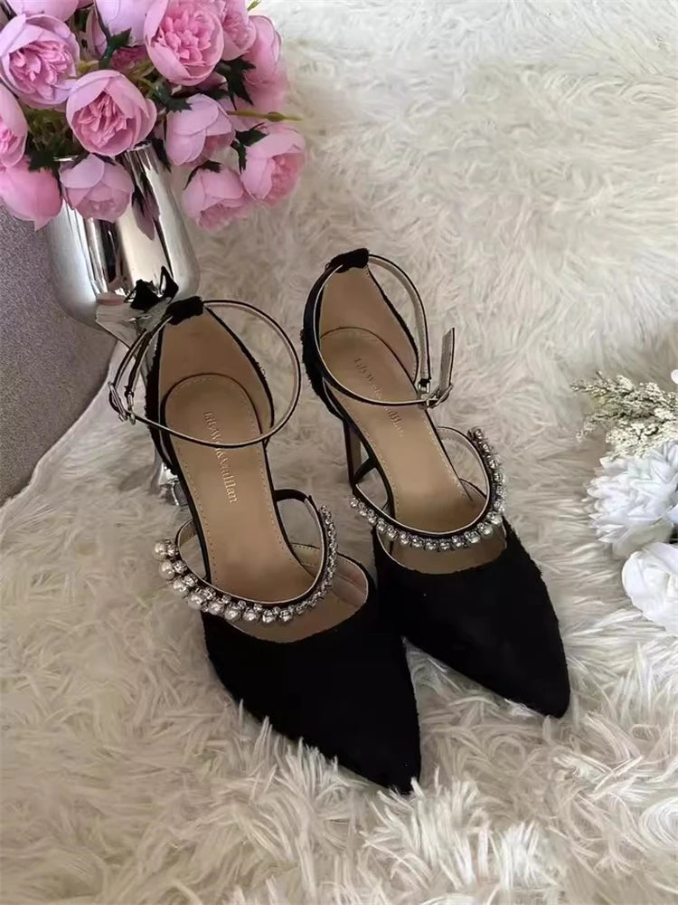 Black high-heeled shoes with pearl embellishments on a white fur surface with pink flowers.