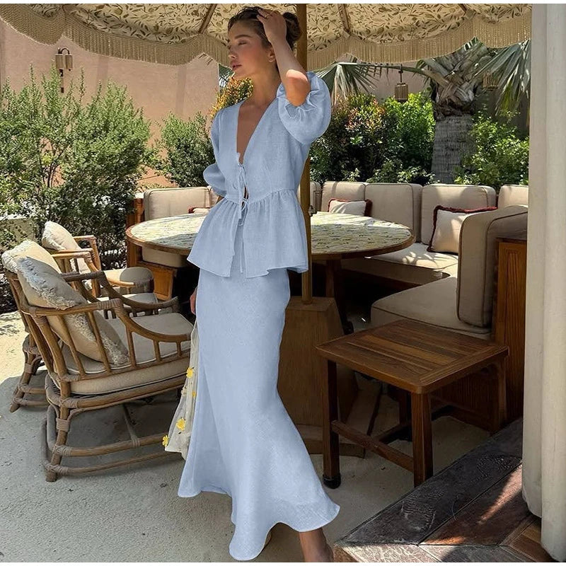 Woman in a light blue dress standing in an outdoor setting with tables and chairs.