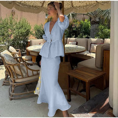 Woman in a light blue dress standing in an outdoor setting with tables and chairs.