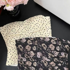 Two folded pieces of fabric, one with black polka dots and the other with floral pattern, on a dark surface.