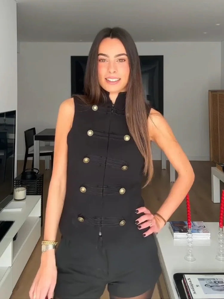 Woman wearing a black sleeveless jacket with gold buttons in a modern kitchen.