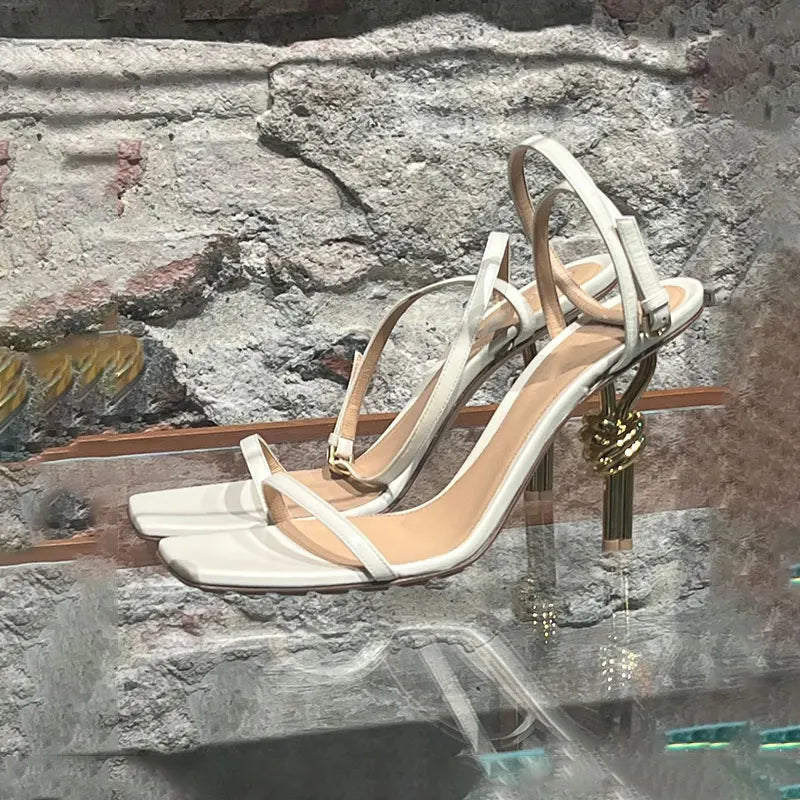 White high-heeled sandals with gold accents on a stone surface