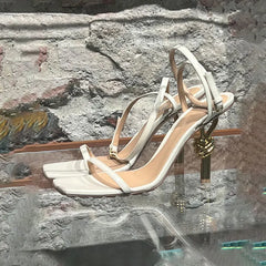 White high-heeled sandals with gold accents on a stone surface