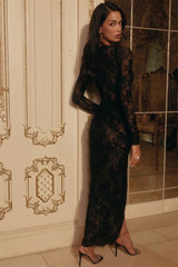 Woman wearing a black lace dress in an elegant room with decorative wall patterns.