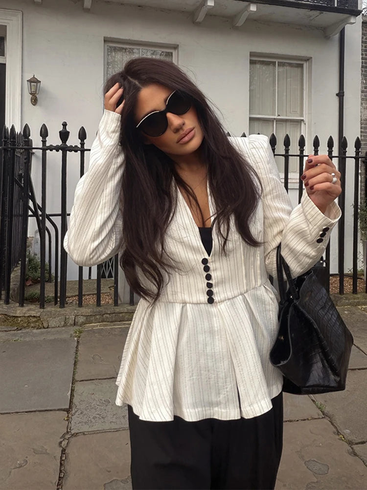 Woman wearing a white peplum top with black buttons, sunglasses, and carrying a black handbag on a street.