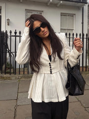 Woman wearing a white peplum top with black buttons, sunglasses, and carrying a black handbag on a street.