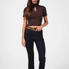 Woman wearing a brown ribbed turtleneck and dark jeans on a white background