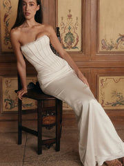 Woman in a strapless white gown sitting on a wooden chair against a decorative wall.
