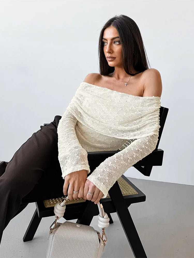 Woman wearing an off-shoulder white top sitting on a chair with a white background