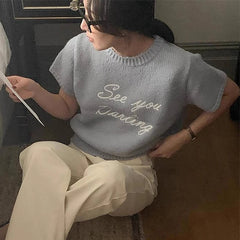 Person wearing a light blue sweater with text, sitting indoors.