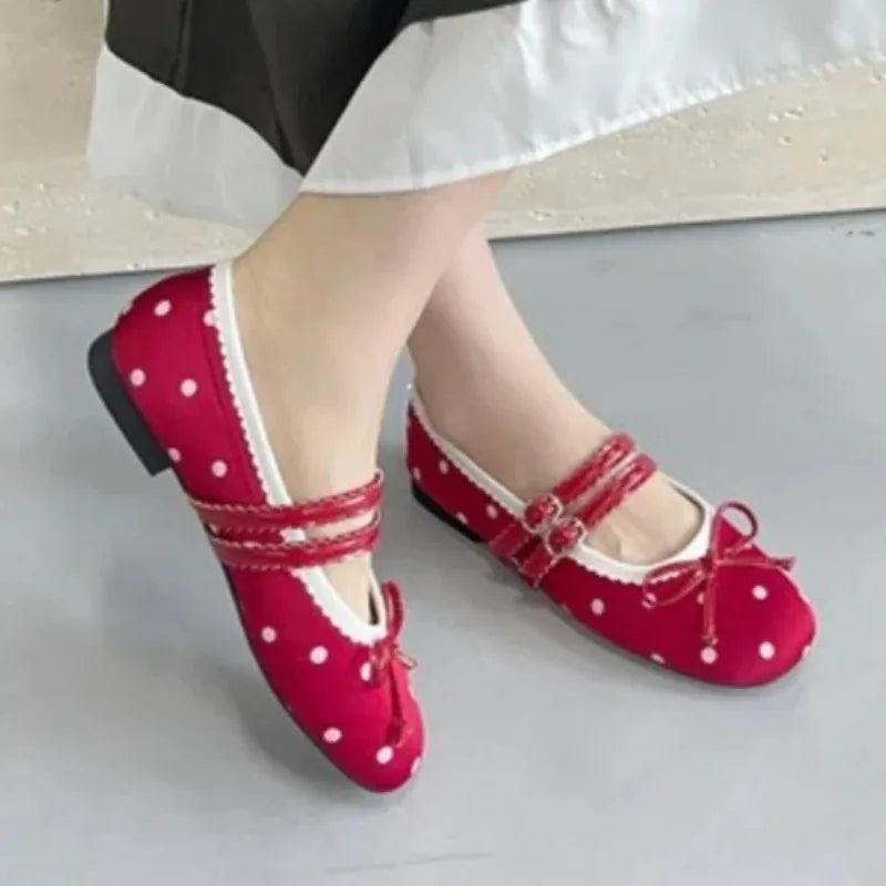 Feet wearing red polka dot ballet flats with white trim and buckle straps