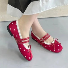 Feet wearing red polka dot ballet flats with white trim and buckle straps